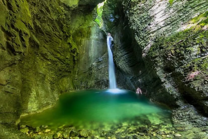 Waterfall plunging into a bright green pool inside a moss-covered rocky gorge, Kozjak Waterfall