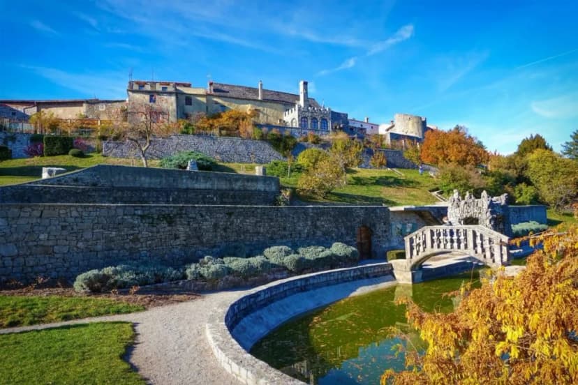 Stone retaining walls, arched bridge, and castle on a hill under a bright blue sky in autumn.