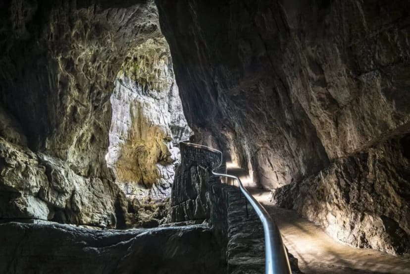 Pathway with metal railing winding through the illuminated interior of Skocjan Caves.