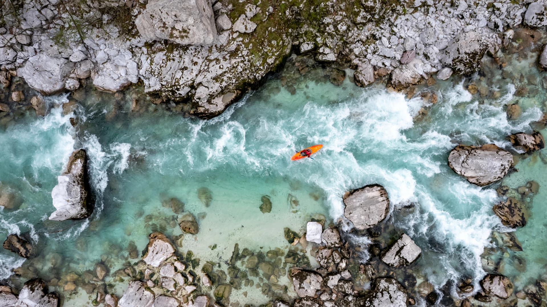 Drone shot of whitewater kayaker dealing with crystal clear rapids of Soca river in Slovenia